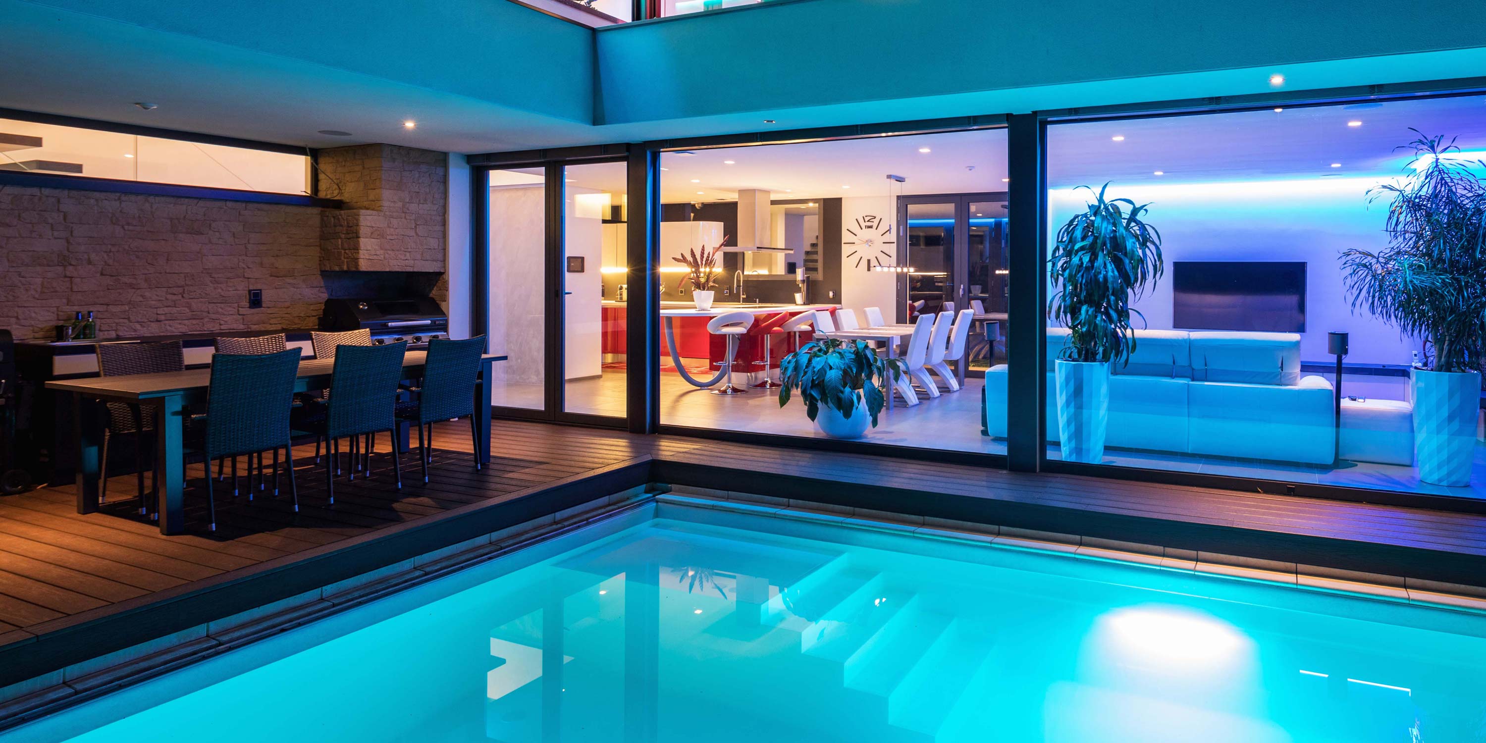 outdoor kitchen of a modern home by a pool and a neon lighted living area