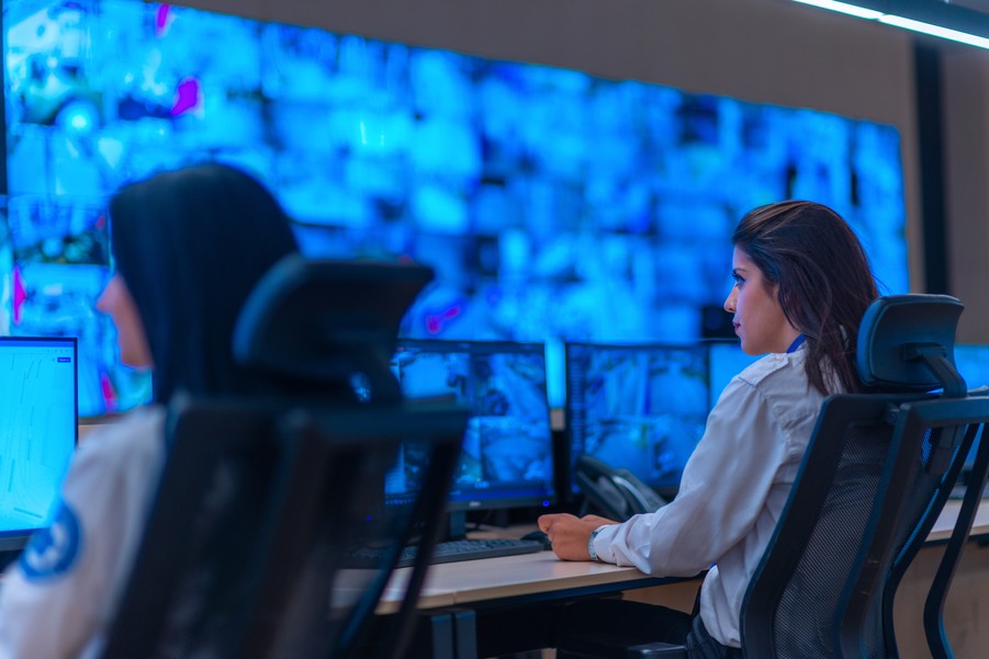 Two security guards watching security camera feeds on several monitors.