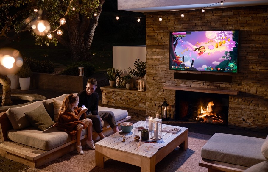 Two people in a home’s outdoor entertainment area with Samsung’s The Terrace outdoor TV above a fireplace.